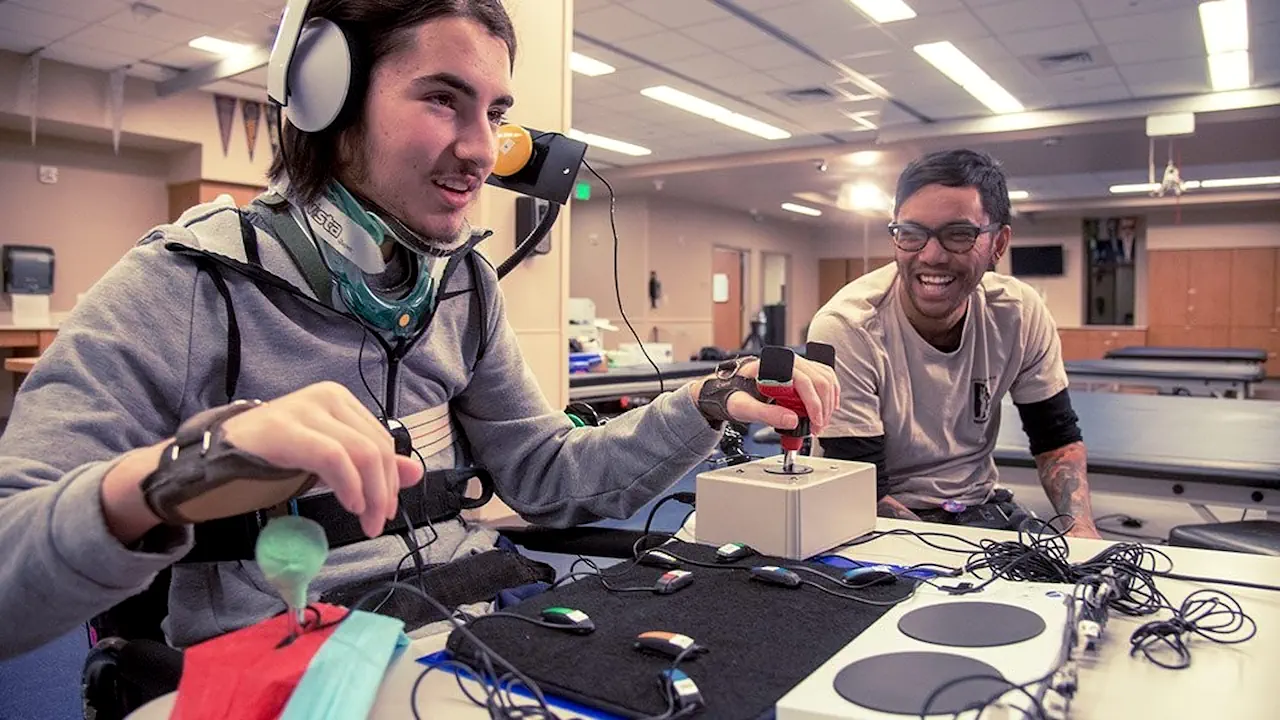 Un jeune homme en situation de handicap teste le Xbox Adaptive Controller, assisté par un professionnel. Ce dispositif conçu par Microsoft facilite l’accès au jeu vidéo grâce à des commandes personnalisables.